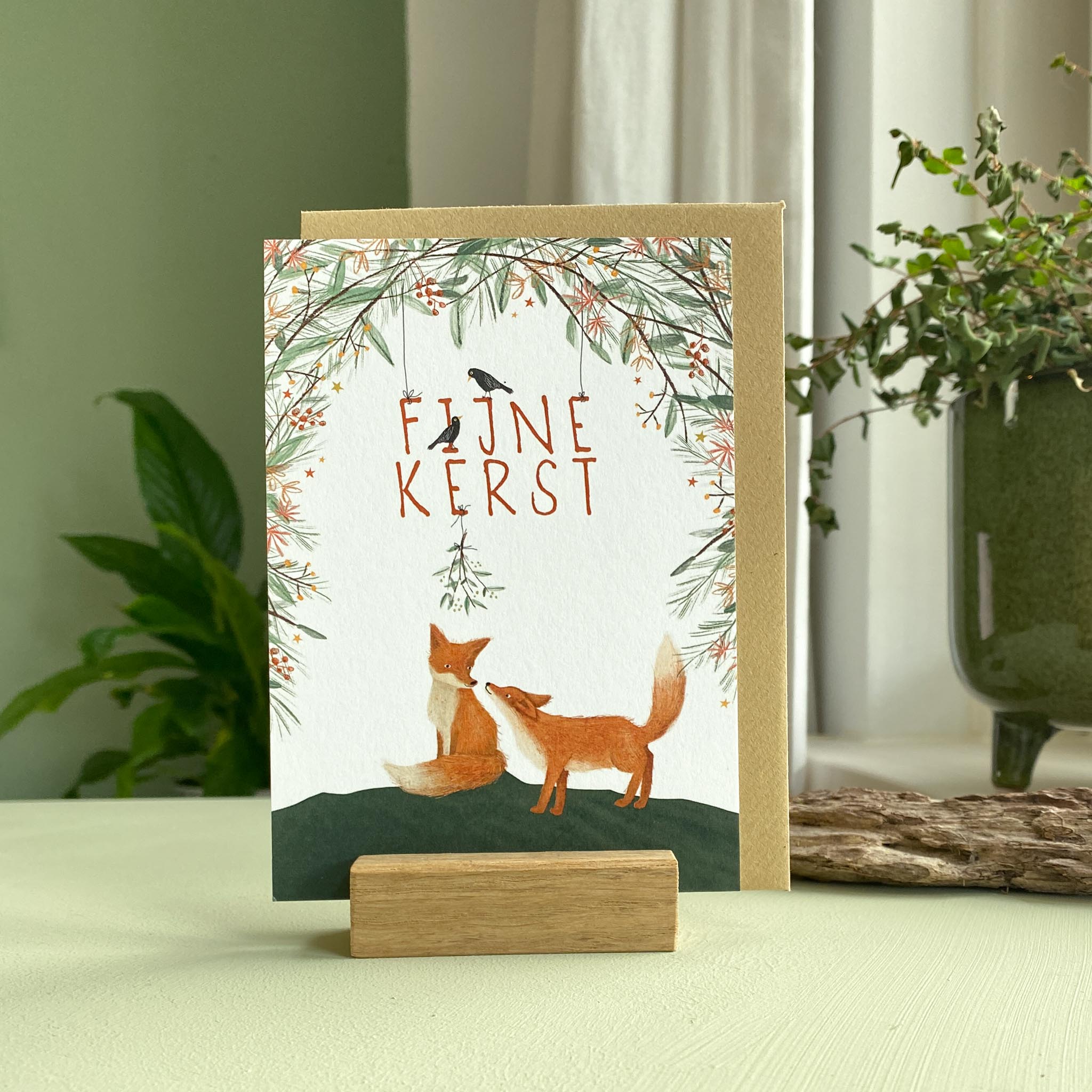 Kerstkaartje met vosjes onder de mistletoe met mooie winterse krans van takken